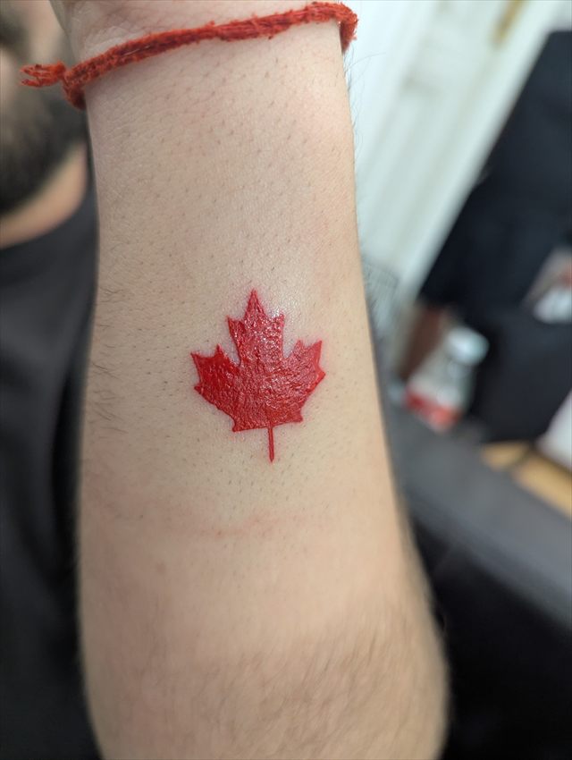 Small red maple leaf tattoo on a forearm