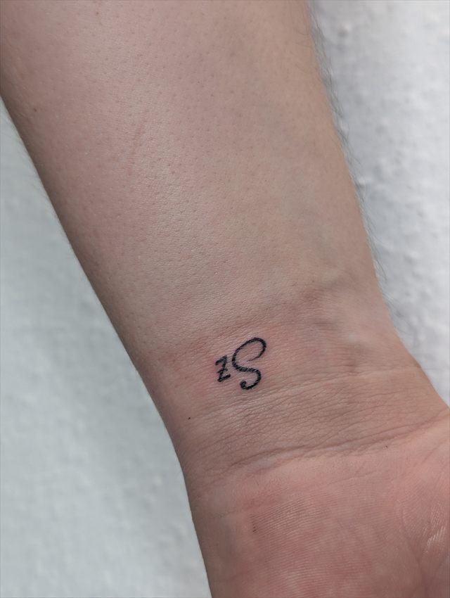 Tiny script initials tattoo on a wrist